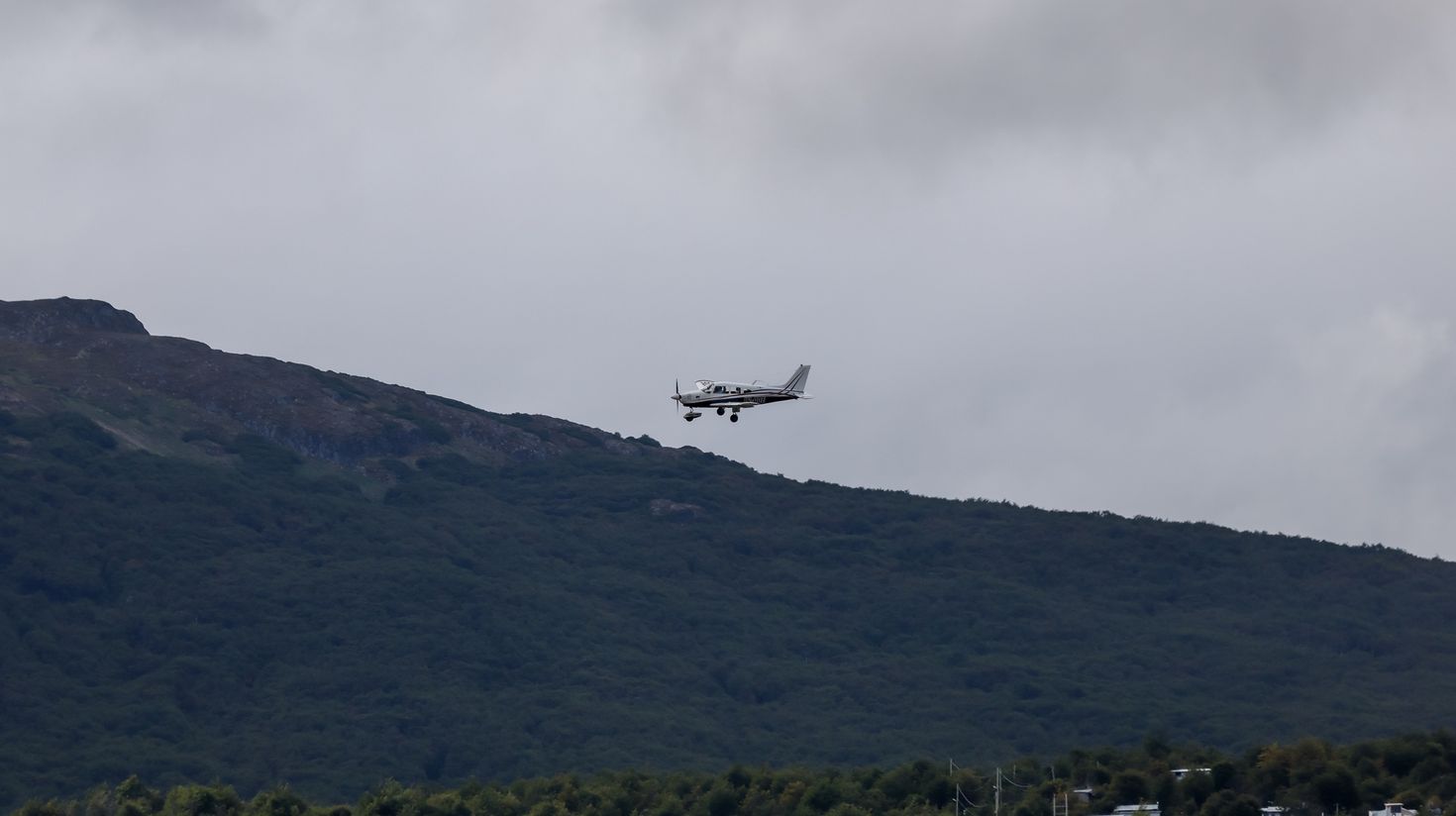 A plane flying above Ushuaia on a cloudy day.
