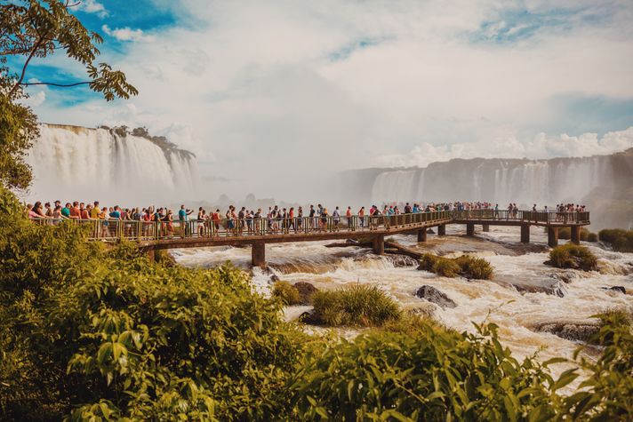 People at a viewing deck built on a river with waterfalls in the background