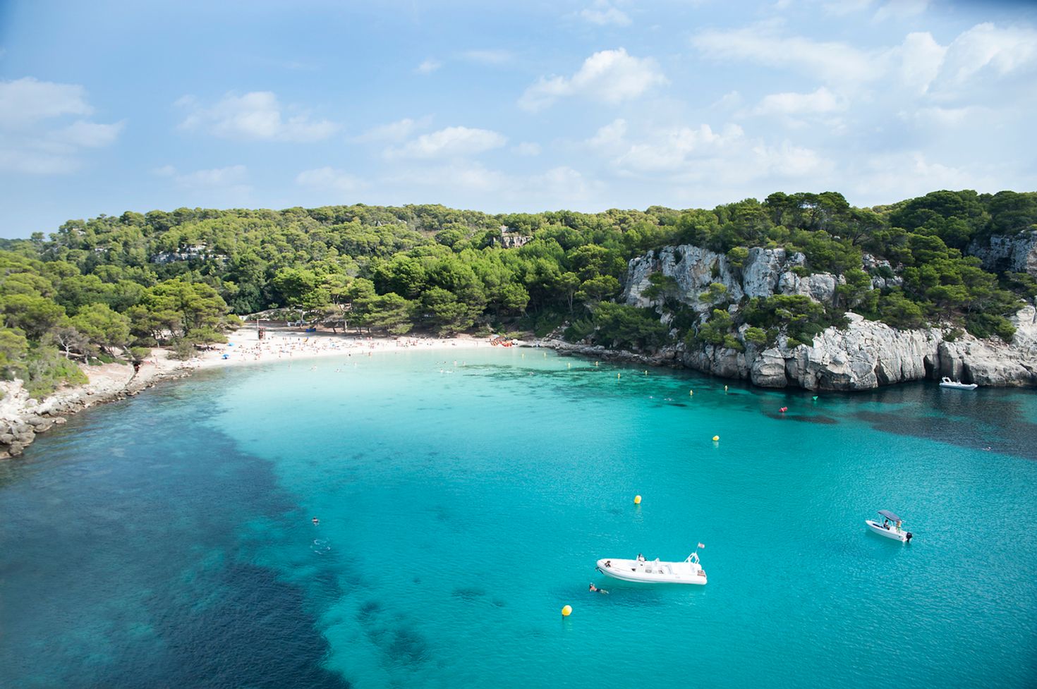 Two boats on the water on Cala Macarella beach surrounded by trees.
