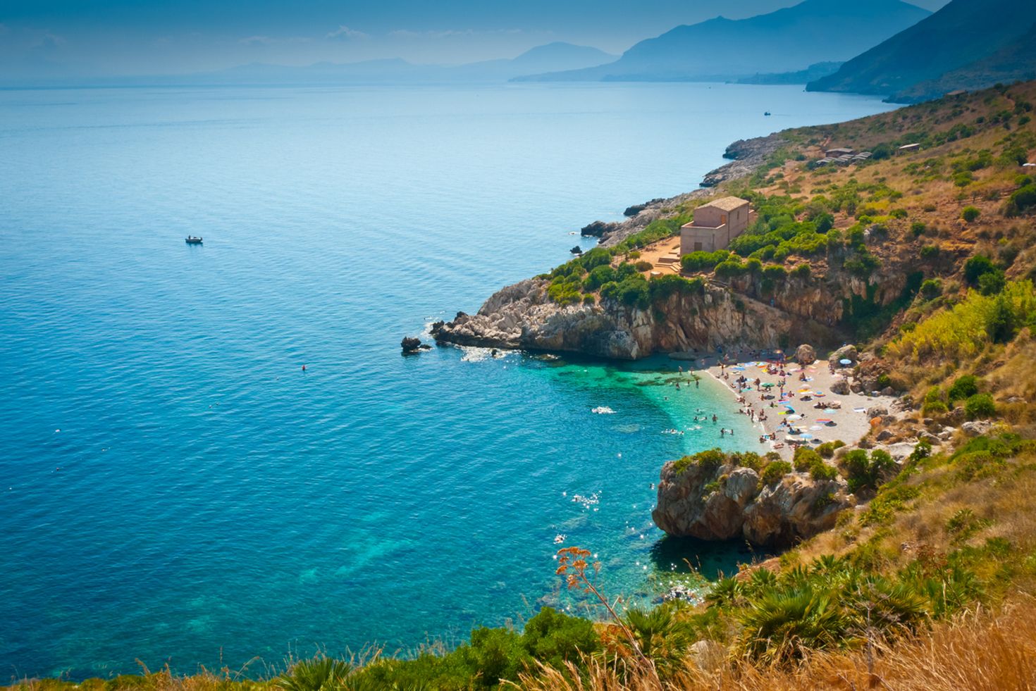 An arial perspective of Zingaro Nature Reserve with blue water, hills, and people enjoying on the beach. 