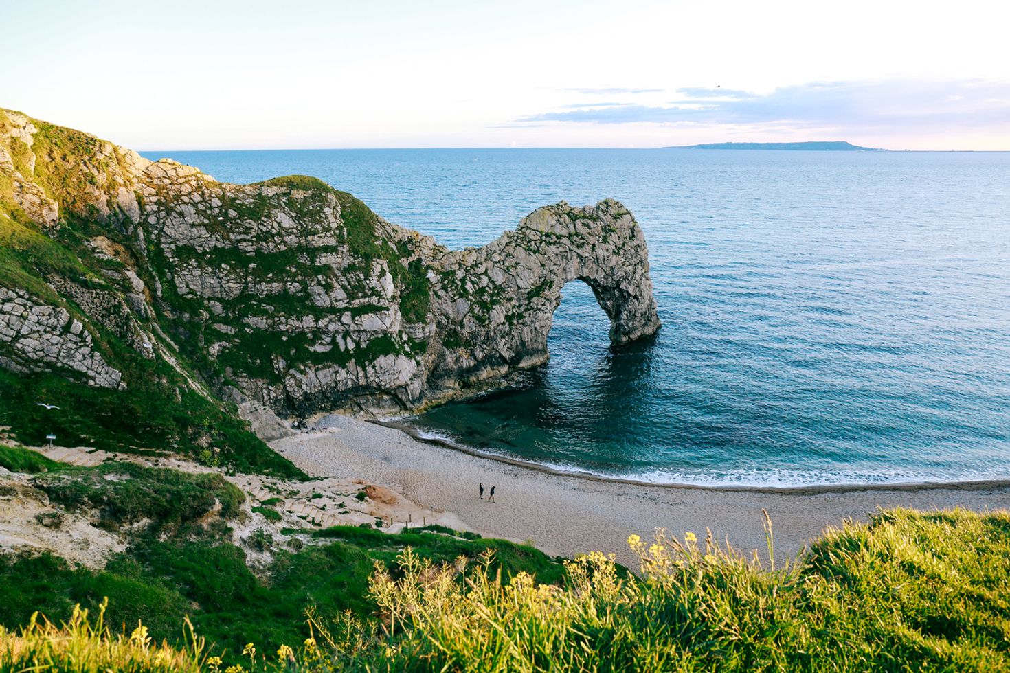 Two people walking on the Durdle door beach overlooking the sea