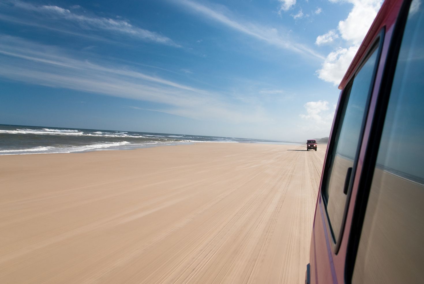 A side car window view with another car in the back overlooking the ocean. 