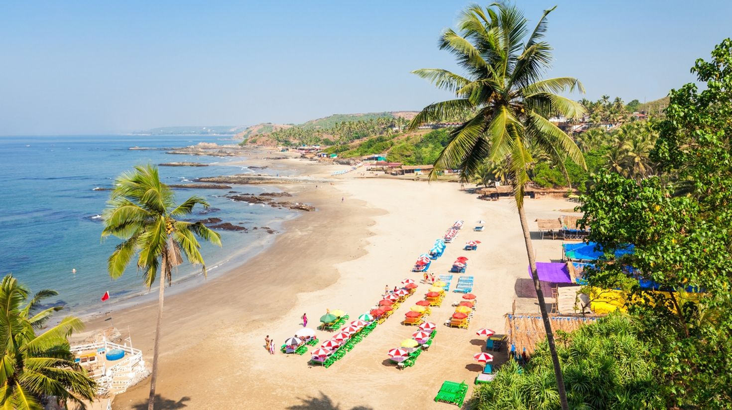An arial view of Patnem beach with colorful sunbeds with trees on one side and water on the other side. 
