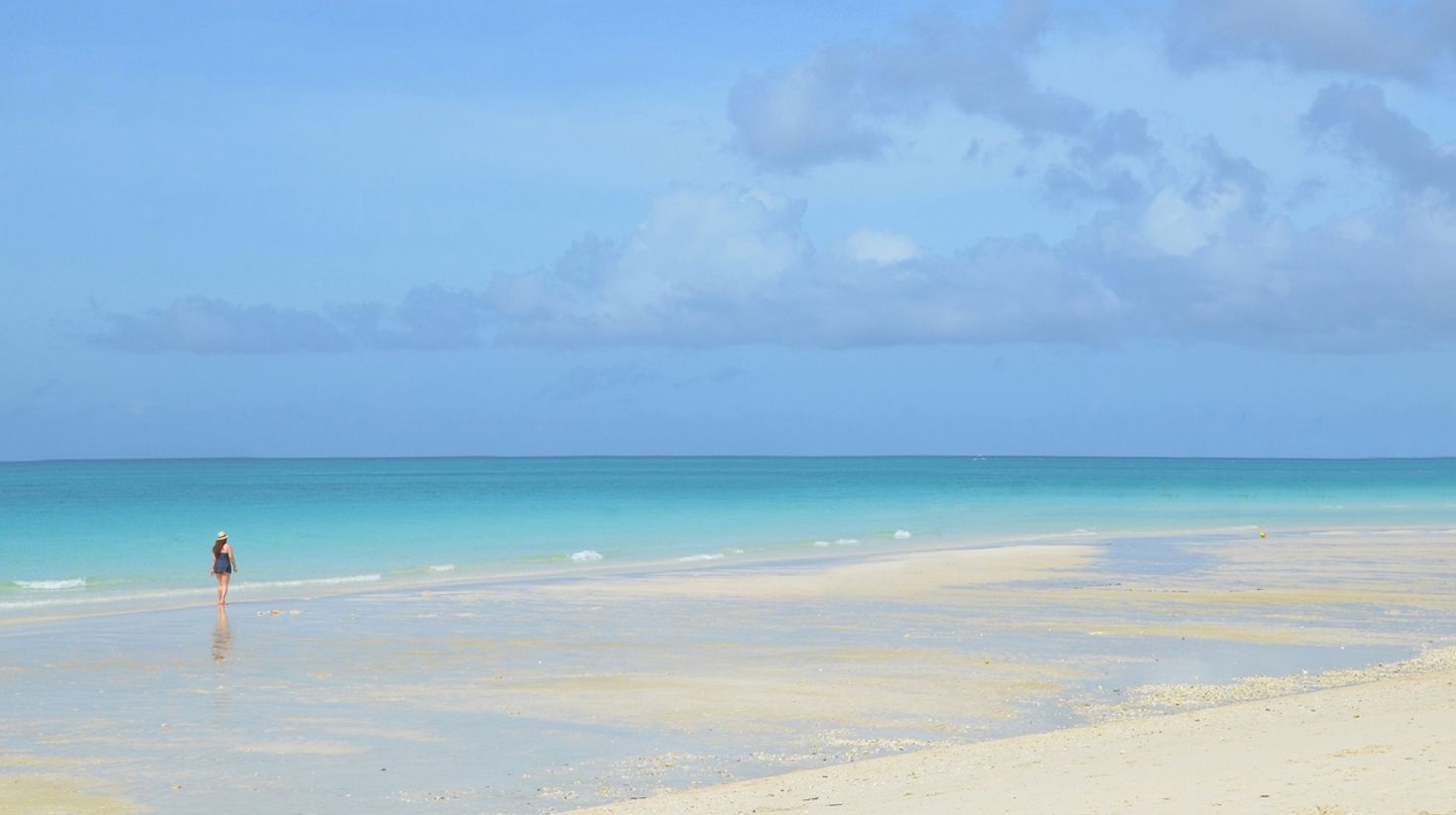 A woman walks on the beach enjoying the clear blue water on a sunny day in White beach on Boracay in the Philippines. 