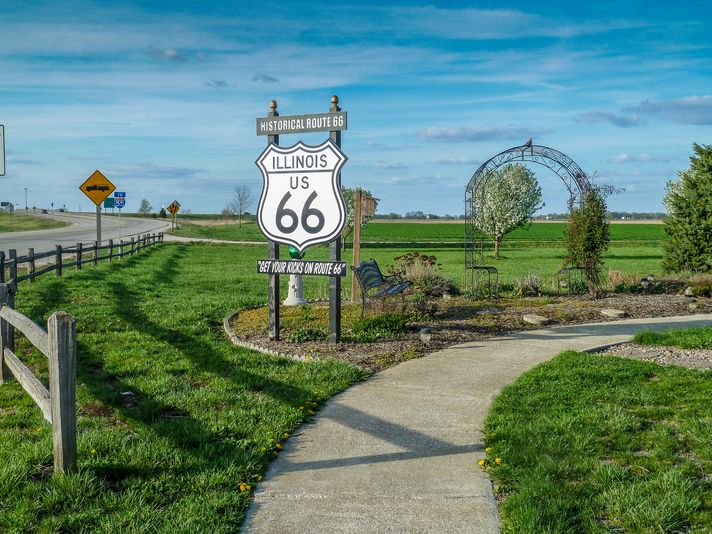 The Route 66 board with a pathway and greenery all around on a clear day in Chicago Illinois.