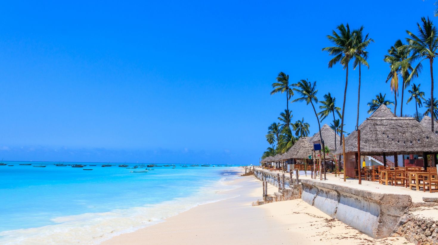 View of the sandy shore, boats, and waters of Nugwi Beach in Zanzibar.