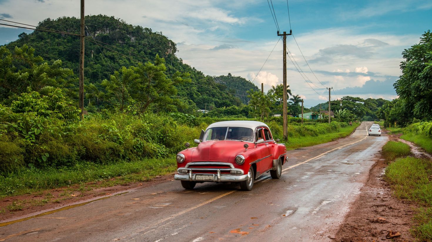 A red retro car driven on the streets of Cuba during the wet season.