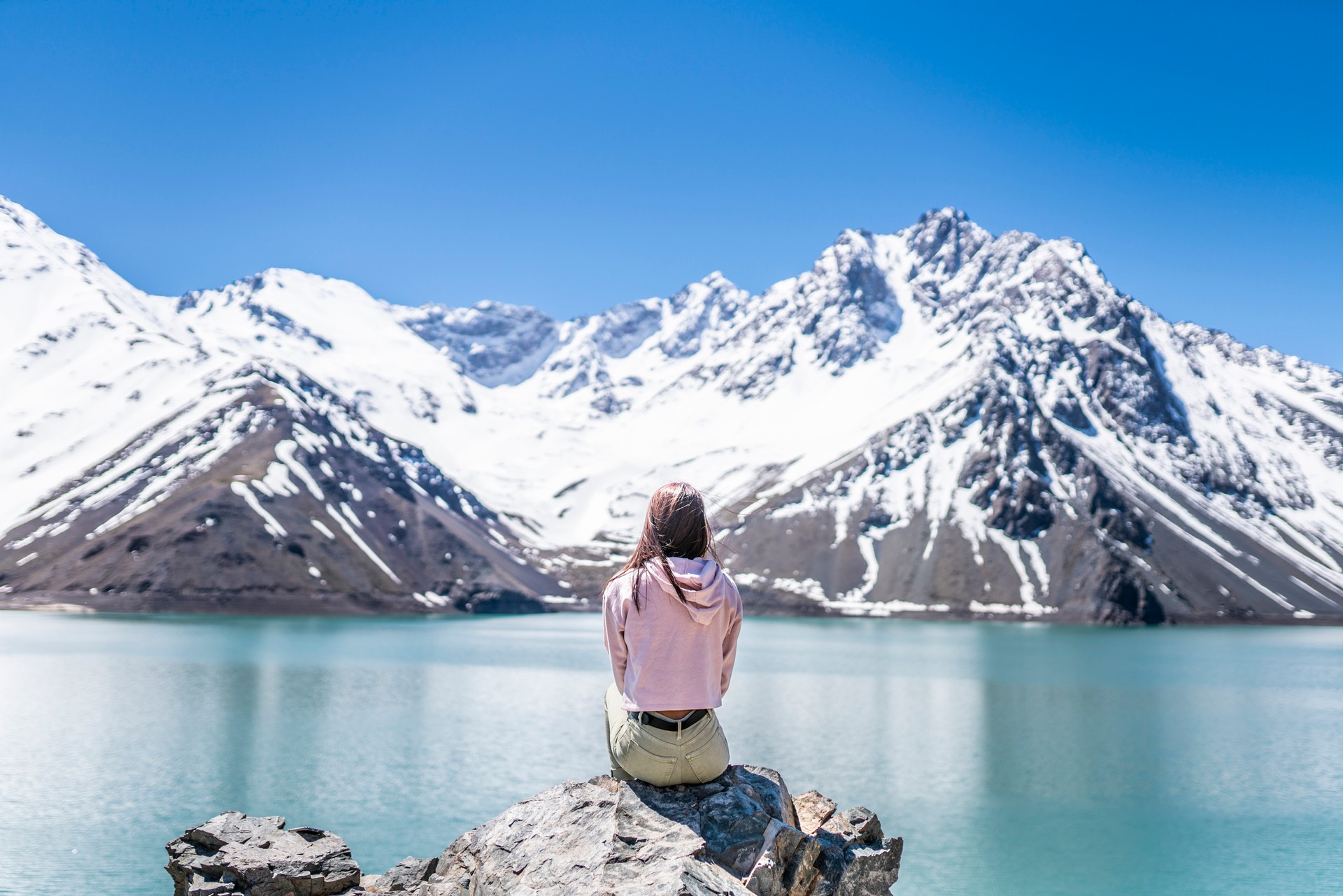 From self-drive tours to guided treks, you have many options during a 10-day trip to Chile. A girl sits on a rock overlooking a blue lake and snow-capped mountains in Cajon del Maipo during a 10-day Chile itinerary
