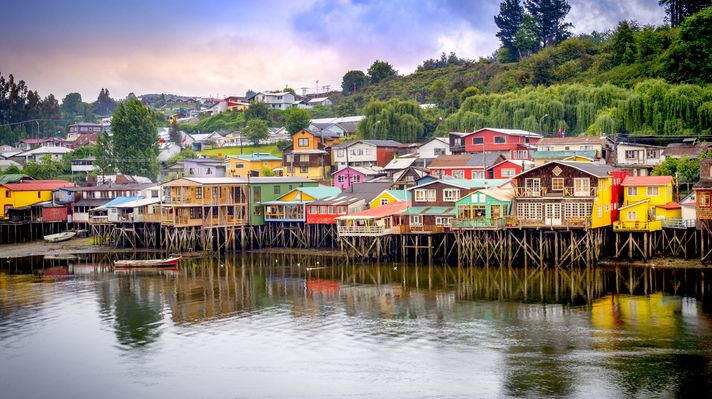 See colorful houses build on wooden struts over a lake in Chiloe while spending 10 days in Chile.