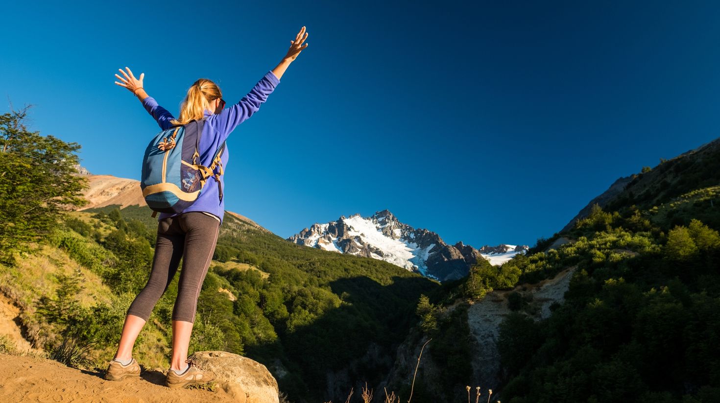 A woman hiker with stretched arms with Chilean mountain on background.