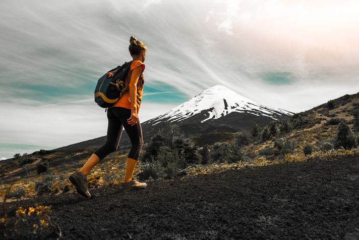 The Villarrica Volcano is popular mostly for the unforgettable climb it offers. But, be warned that this hike isn’t an easy task. A woman hiking up a trail next to a snow-capped volcano