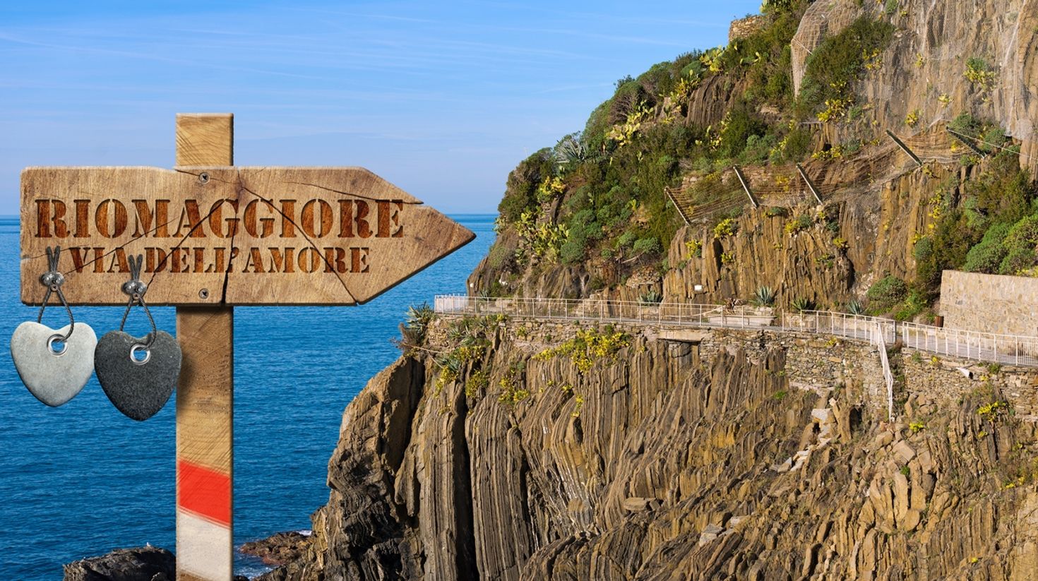 A wooden board pointing direction to Riomaggiore via Dell' Amore with its trail in the hills in Italy. 