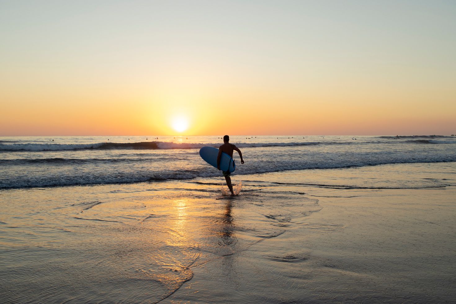 A surfer racing towards the ocean during sunset at Nosara, Costa Rica
