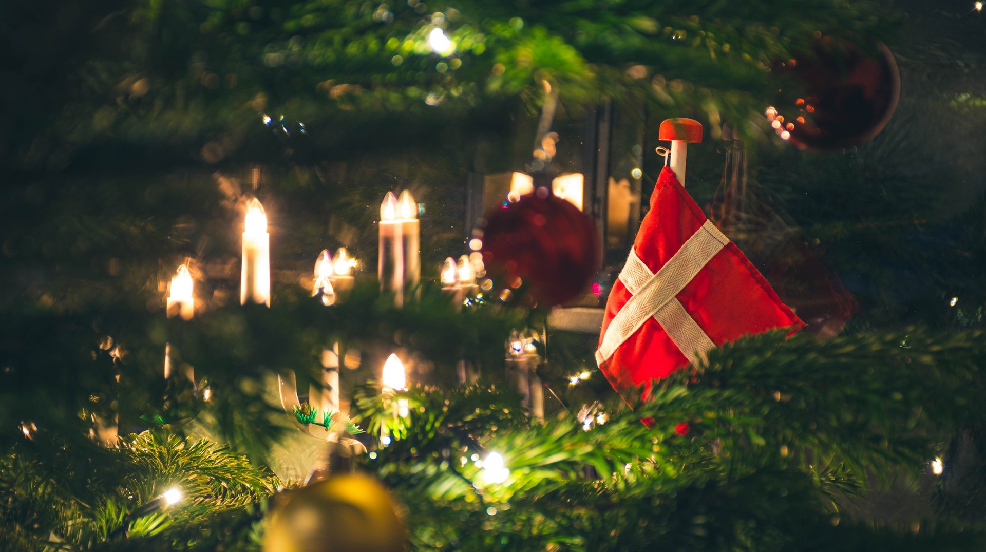 Visit Denmark in December to embrace its hygge-style Christmas spirit, cozying up to pubs or sipping a cup of hot cocoa by the fireplace. A closeup shot of Christmas tree with a Danish flag ornament taken in Denmark in December.