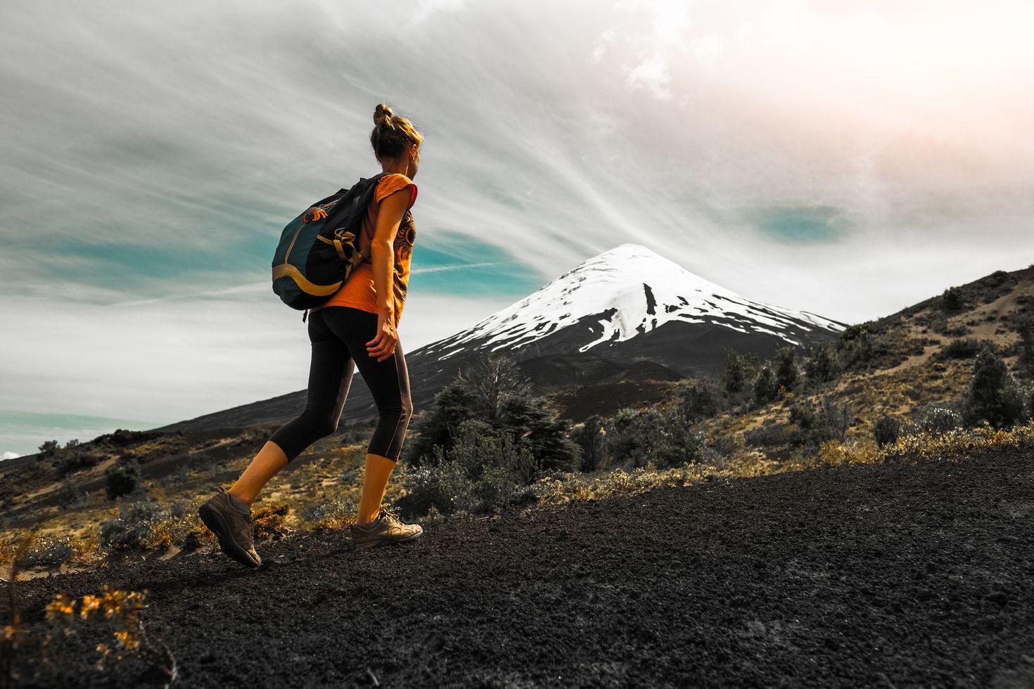 A woman hiking up a trail next to a snow-capped volcano