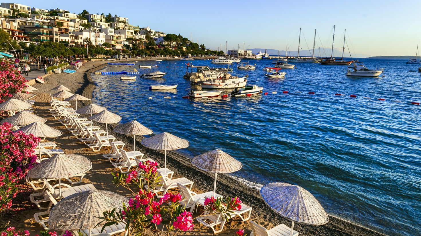 A beach at Bodrum along the Aegean coast with ships, flowers and beach umbrellas.