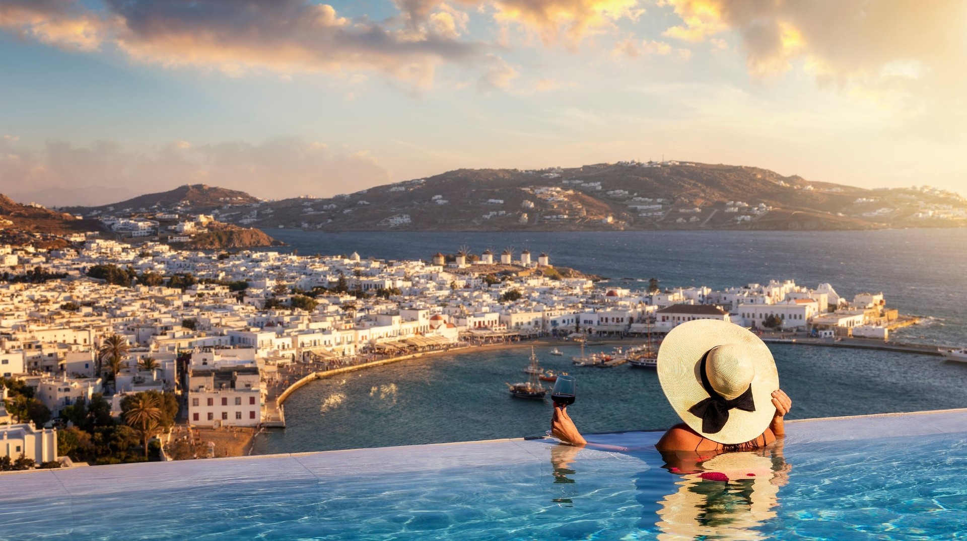 Enjoy Mykonos Island during your 12 days in Greece and soak up its vibrant nightlife, stunning beaches, and charming streets A woman with a glass of wine enjoying the view of Mykonos Island during her 12 days in Greece.