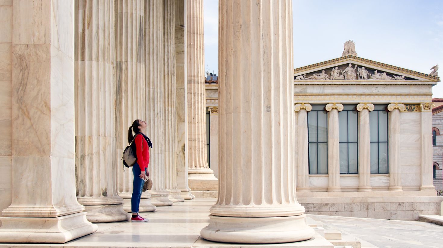 A girl looks up at the ceiling, under the columns of the Athenian Academy