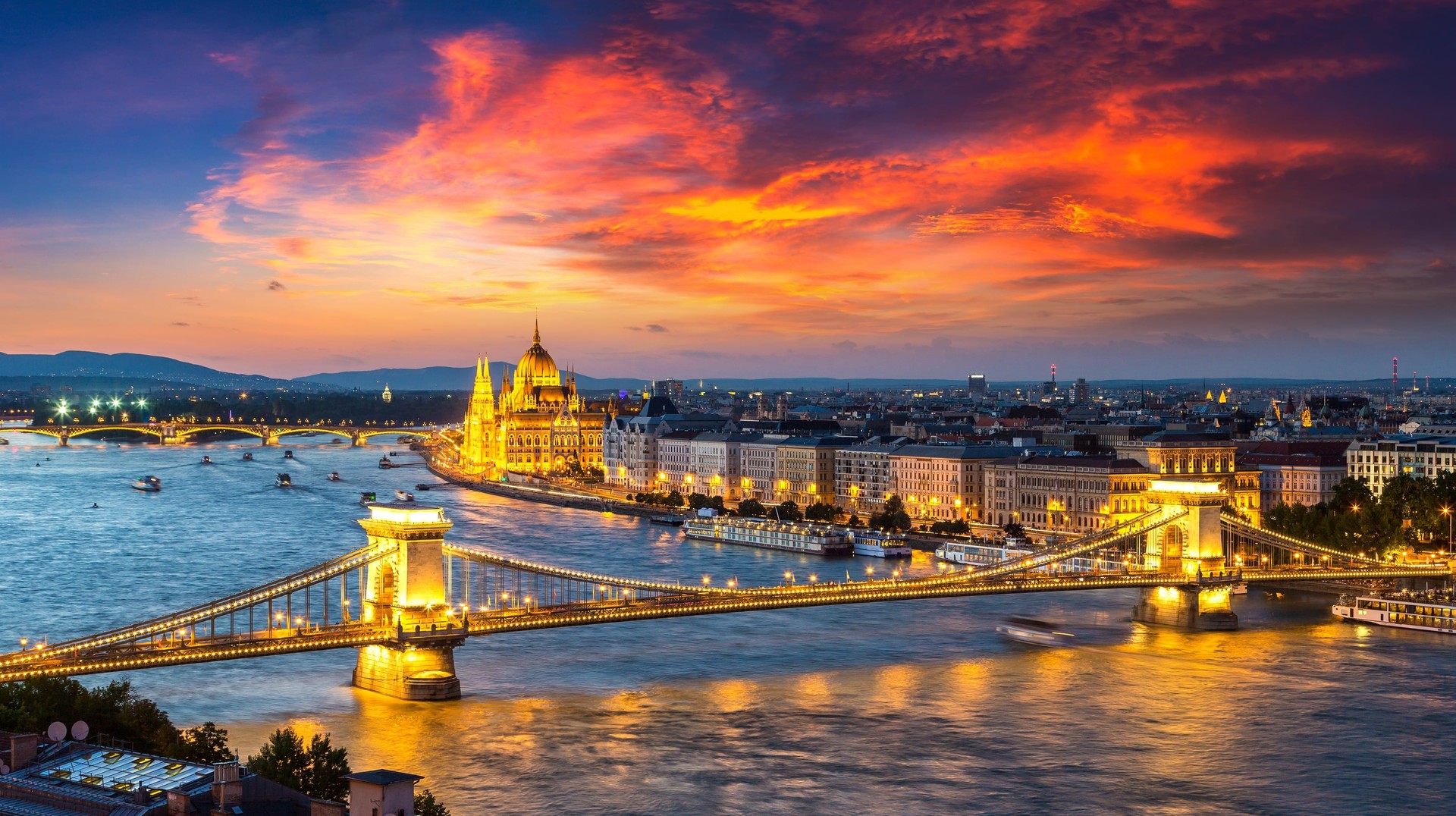 With love in the air, romantic river cruises in the Danube are popular in Hungary in February. Danube under red sky and brightly lit Budapest city in Hungary in February.