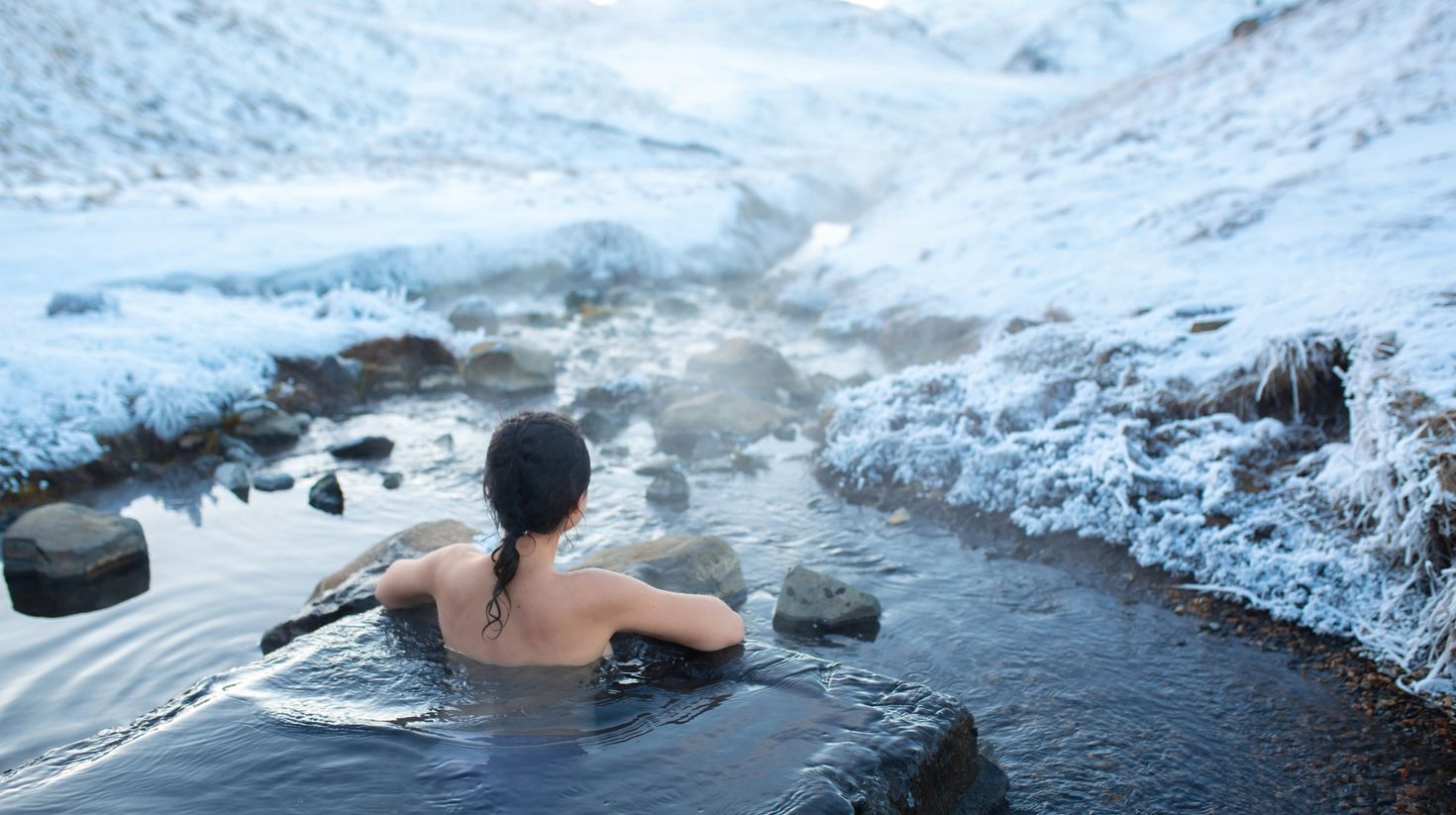 The girl bathes in a hot spring with a view of the mountains in Iceland
