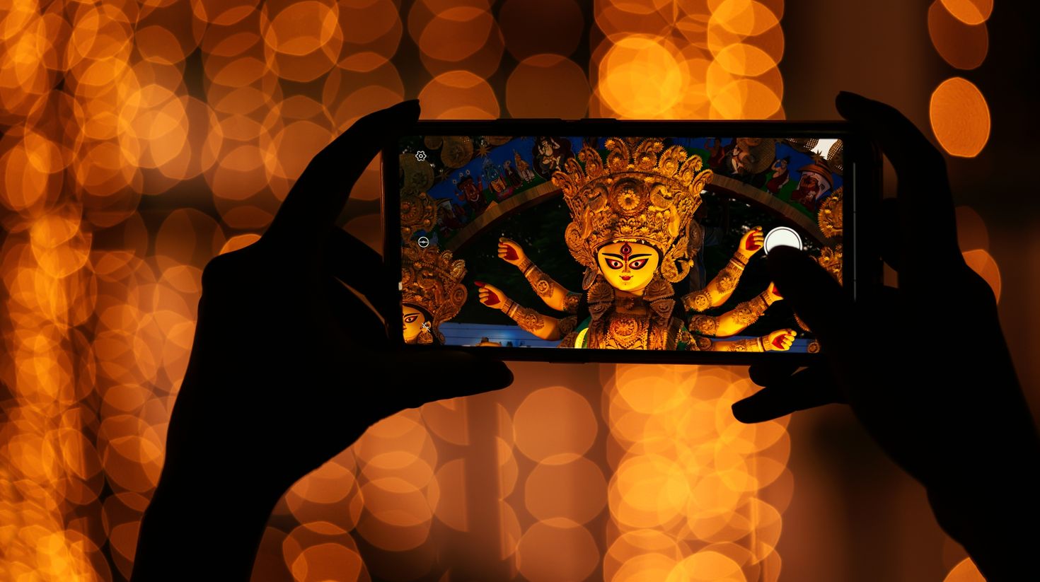 Hand holding mobile phone and taking photos of Goddess Durga idol