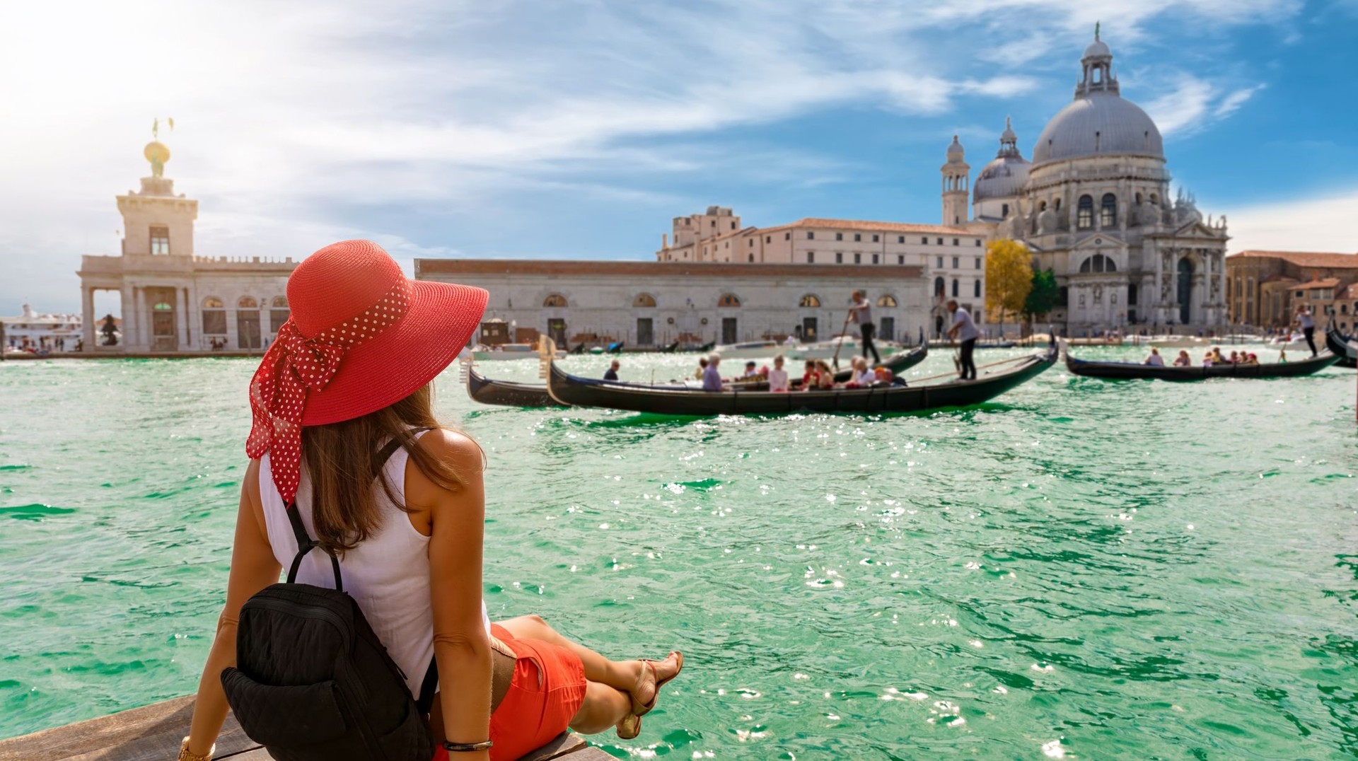 Add a touch of magic to your 5 days in Italy with a visit to this timeless city of canals, romance, and unparalleled beauty of Venice. A girl looking at Canal Grande in Venice with a group of people in a boat during her 5 days in Italy.