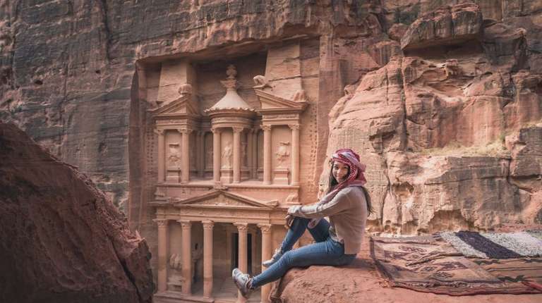 A tourist girl smiling sitting on the rock in front of Treasury during her 4 days in Jordan.