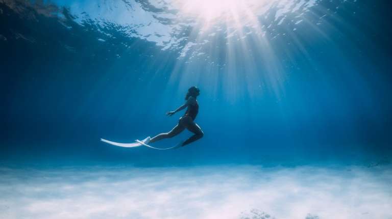 Freediver with white fins glides and posing underwater in ocean in Mexico in April.