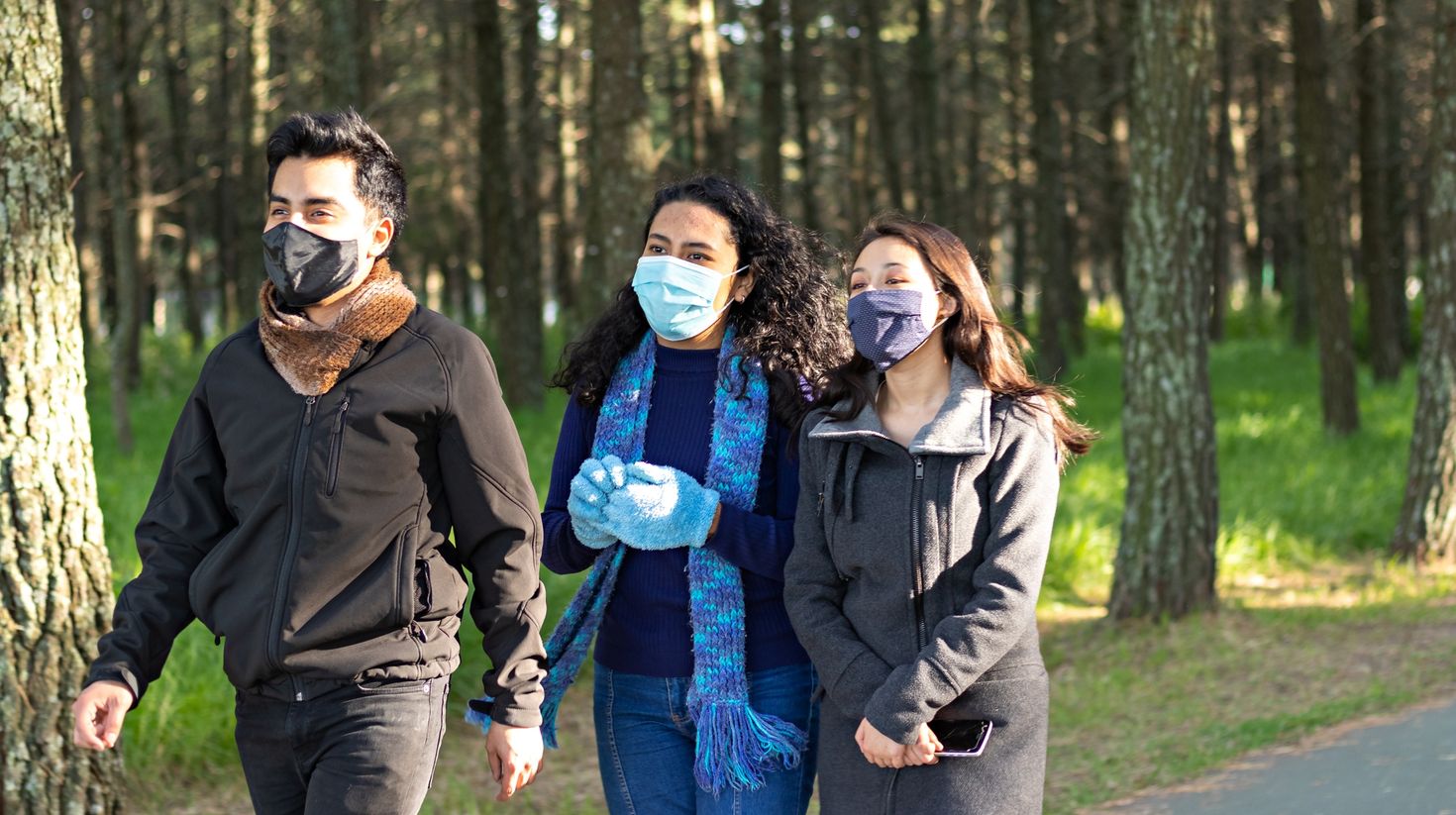 group of friends, two women and a man, wearing mask while walking in a park