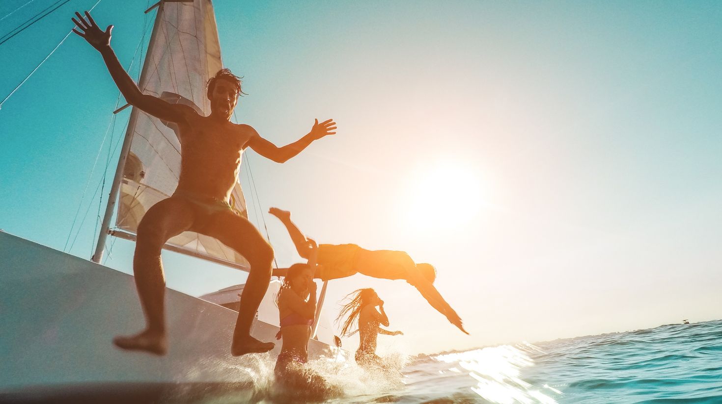 friends diving from sailing boat into the sea