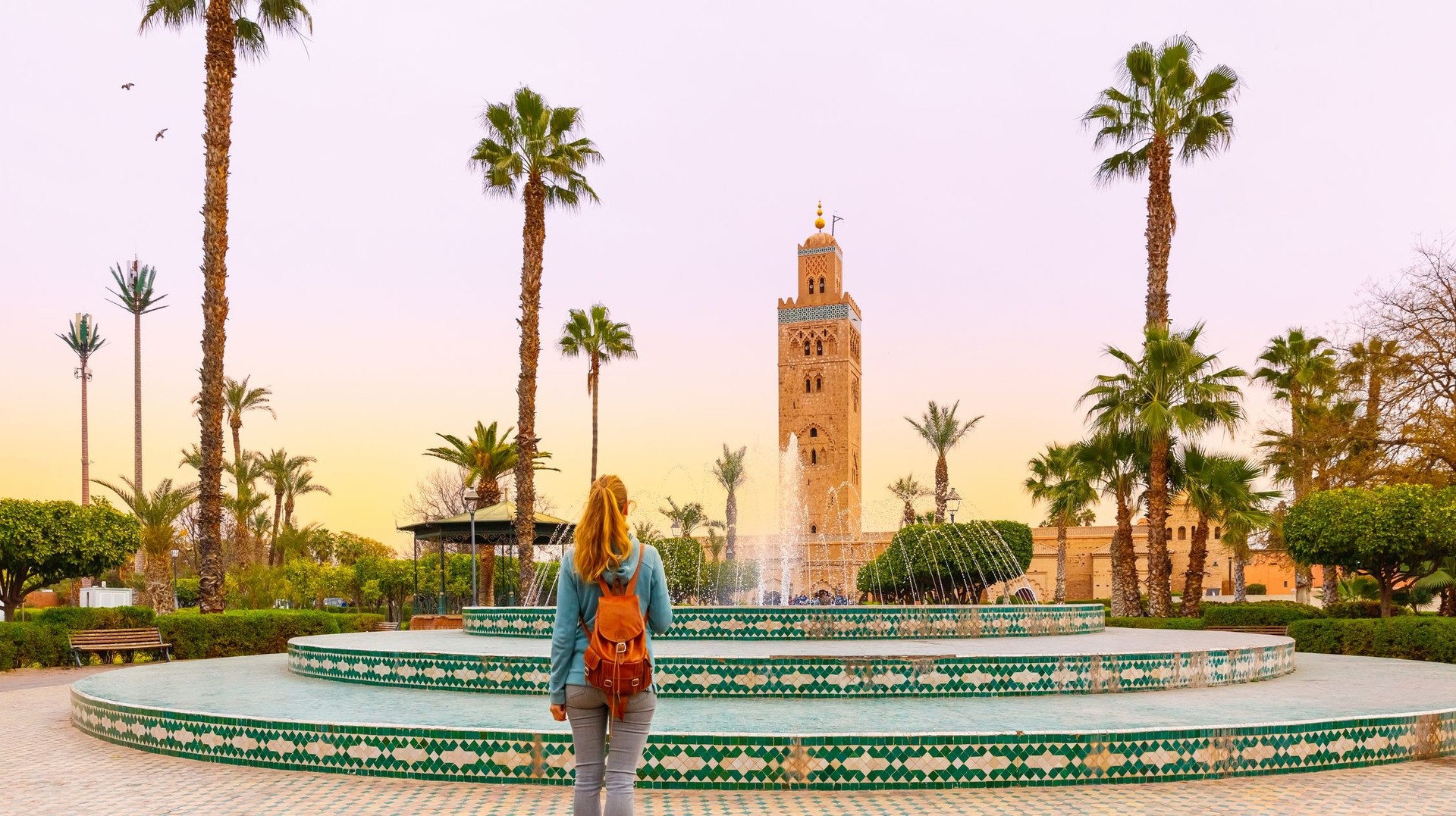 Visit the iconic Koutoubia Mosque during your 4 days in Morocco, where stunning architecture and rich history make it an unmissable highlight of Marrakech. A woman tourist looking at Koutoubia mosque during dusk on her 4 days in Morocco.