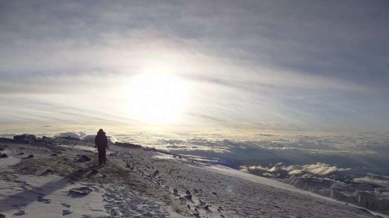 A hiker on a snow-covered mountain trail with a stunning view of cloud-covered valley below.