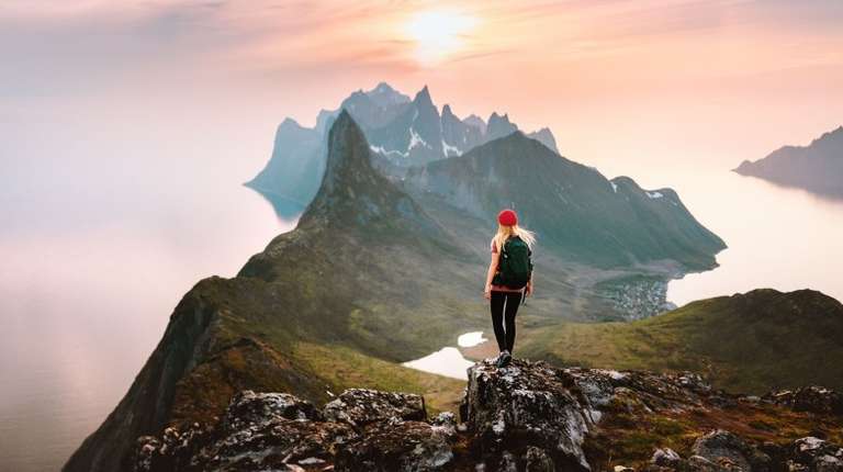A woman hiker solo in the mountains enjoying the sunset view on Senja Island on her 12 days in Norway.