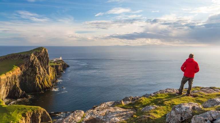A man admiring the view of lighthouse in Isle of Skye which is one of the best places to visit in Scotland.