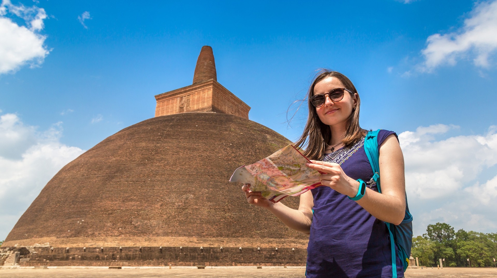 Woman holding map in front of Abhayagiri temple, one of the places to visit in Sri Lanka during a clear day.