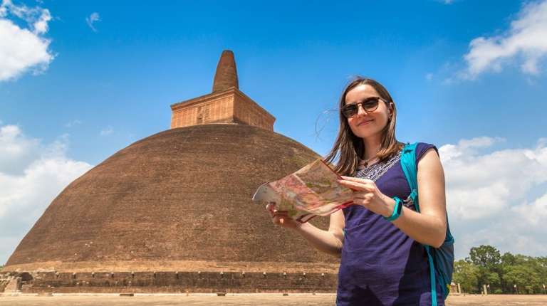 Woman holding map in front of Abhayagiri temple, one of the places to visit in Sri Lanka during a clear day.