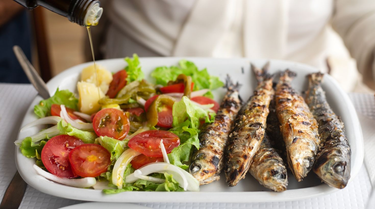 Grilled sardines with salad and olive oil on white dish stock