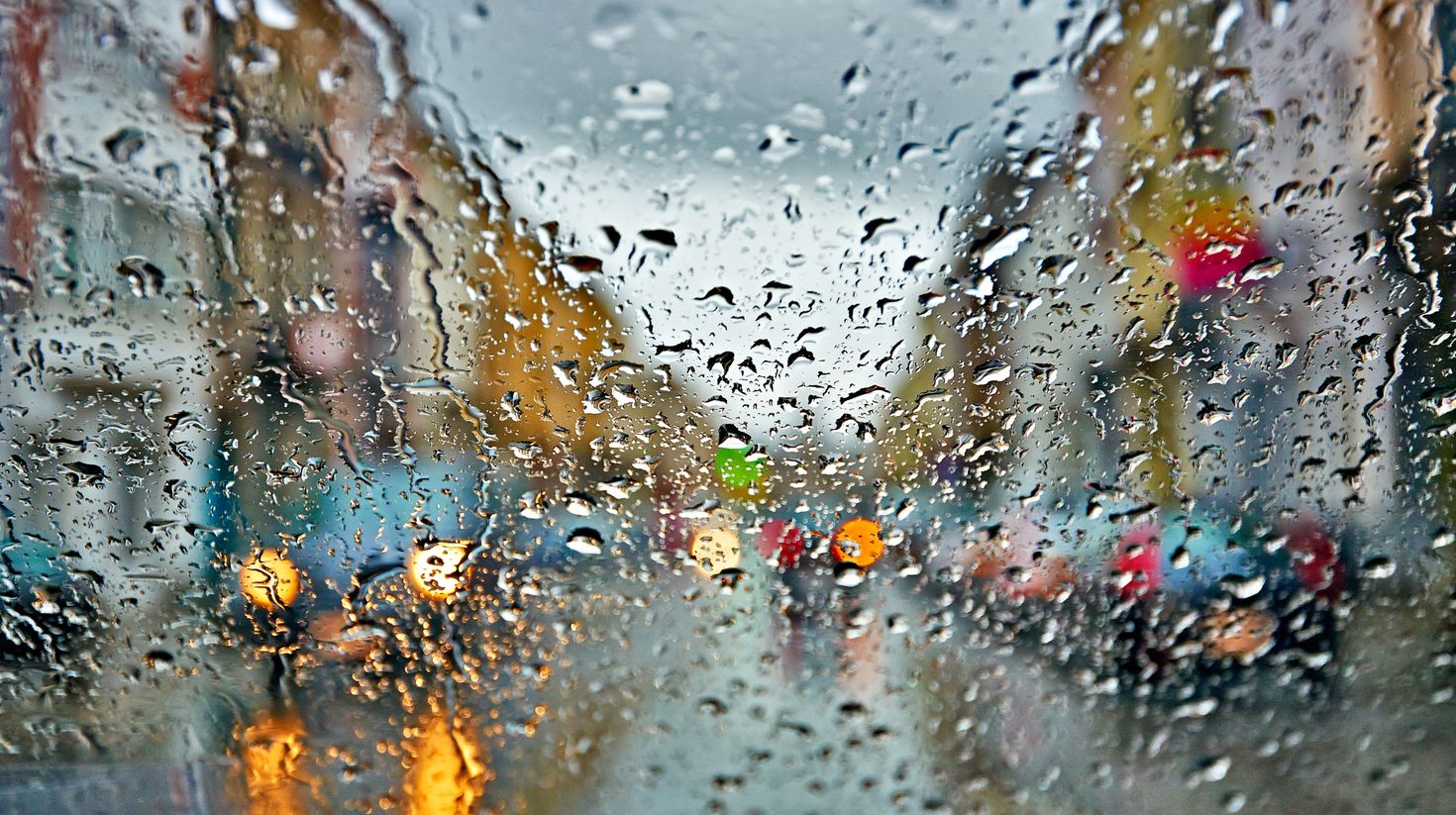 Car windshield with rain drops during storm and blurred stoplights.