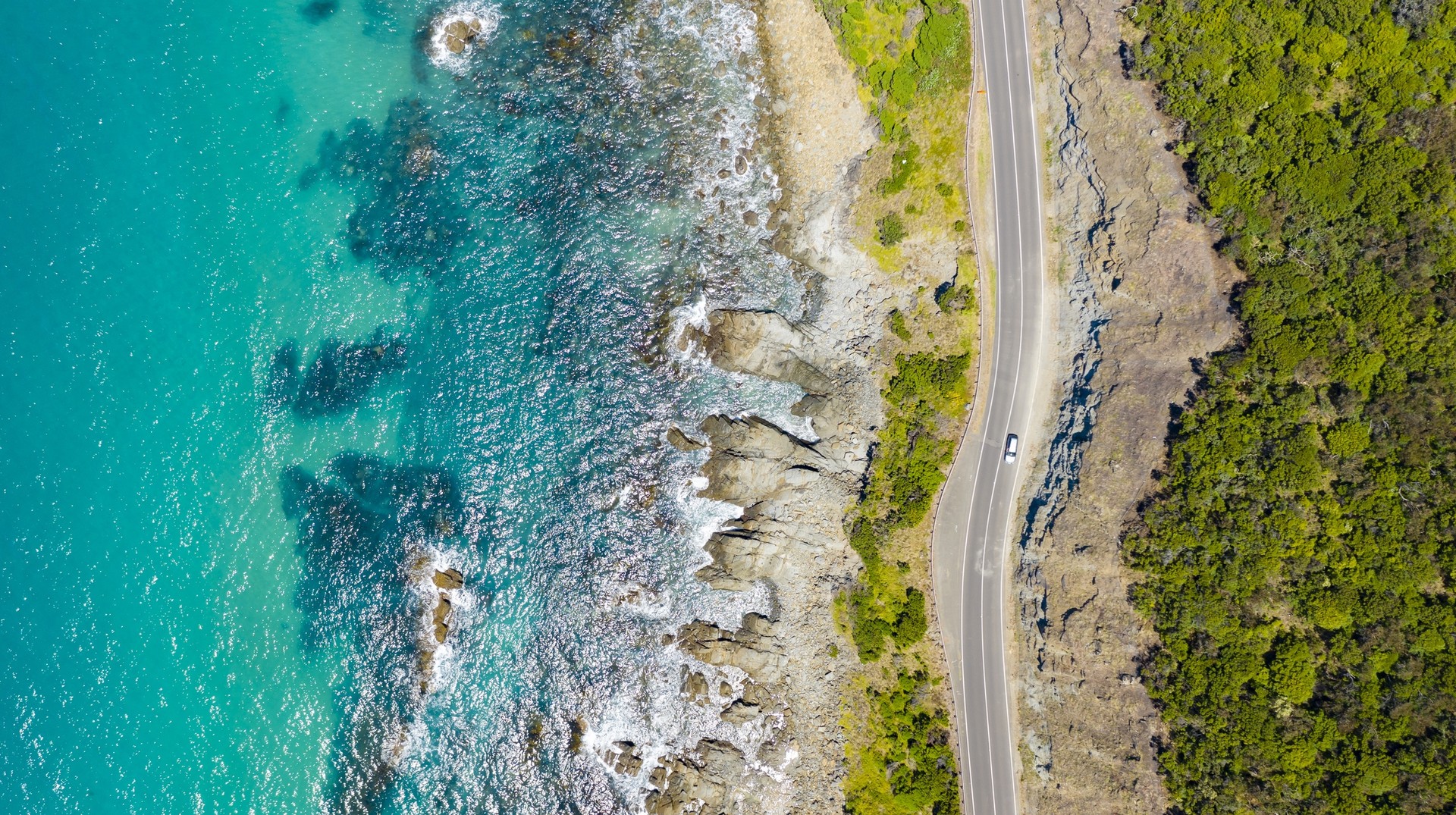 Driving along the Great Ocean Road in Australia is one of the best ways to see the country. An aerial view of a section of Great Ocean Road with the turquoise waters on one side and the green forest on another.