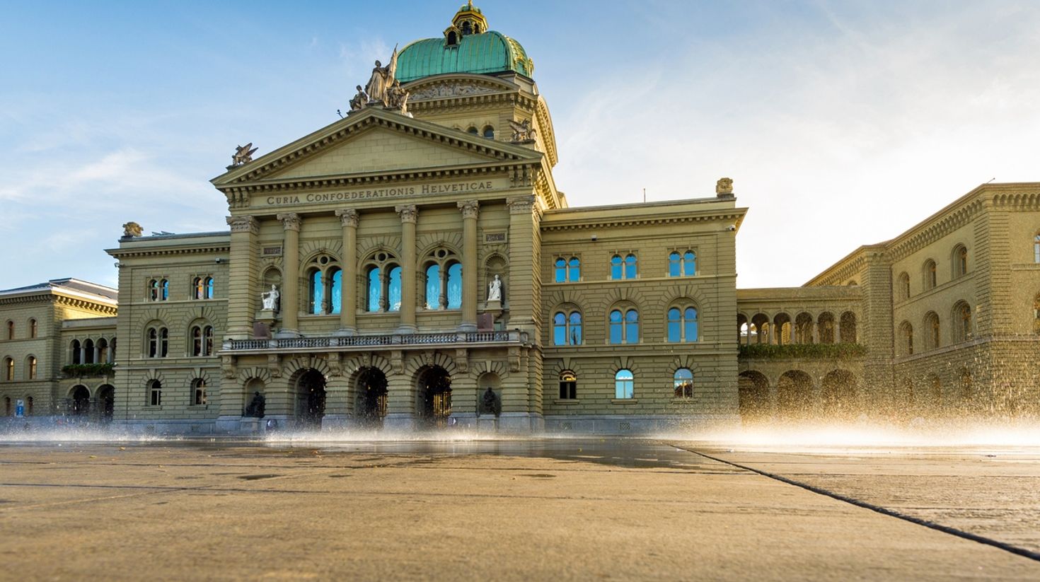A view of the Bern Federal House of Parliament with water sprinkles in front of it.