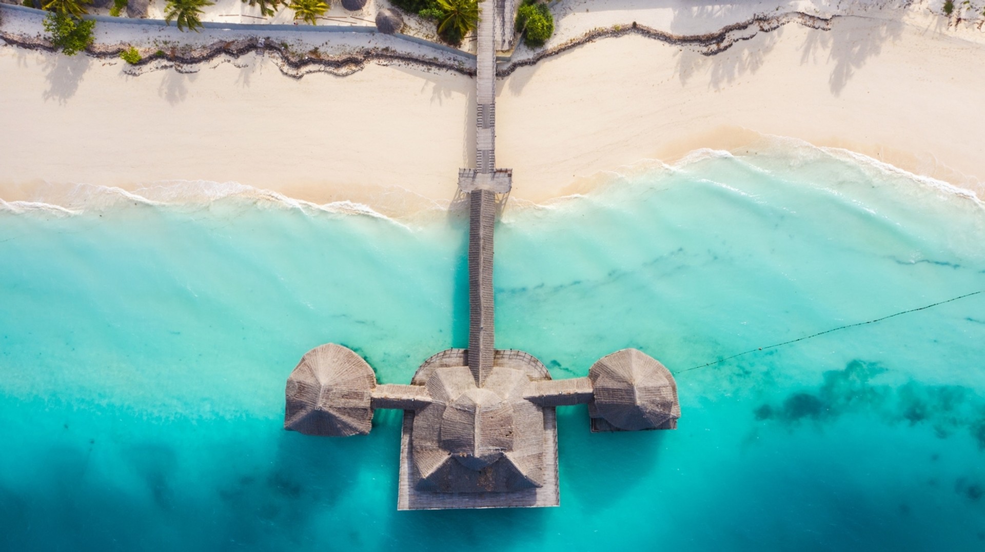 Take in the refreshing wind from the turquoise waves while relaxing on the white sandbank beach on Zanzibar island in Tanzania in November. A beach resort built on the shorelines of blue sea water in Tanzania in November.