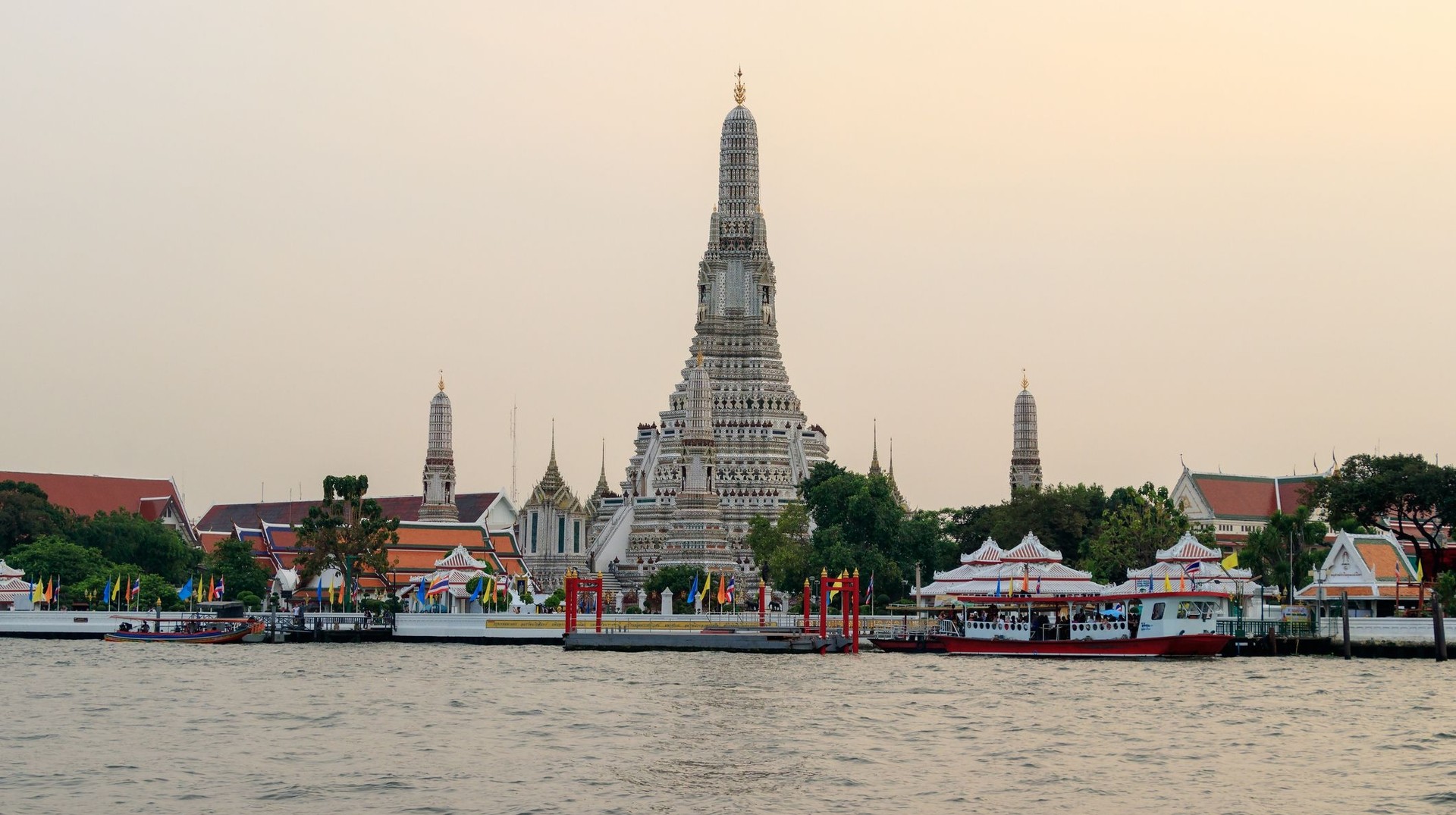 Discover the beauty of Thailand in May by exploring its majestic temples and enjoying indoor activities to escape the tropical rains. The front view of Wat Arun Temple with Chao Phraya River on a cloudy day in Thailand in May.