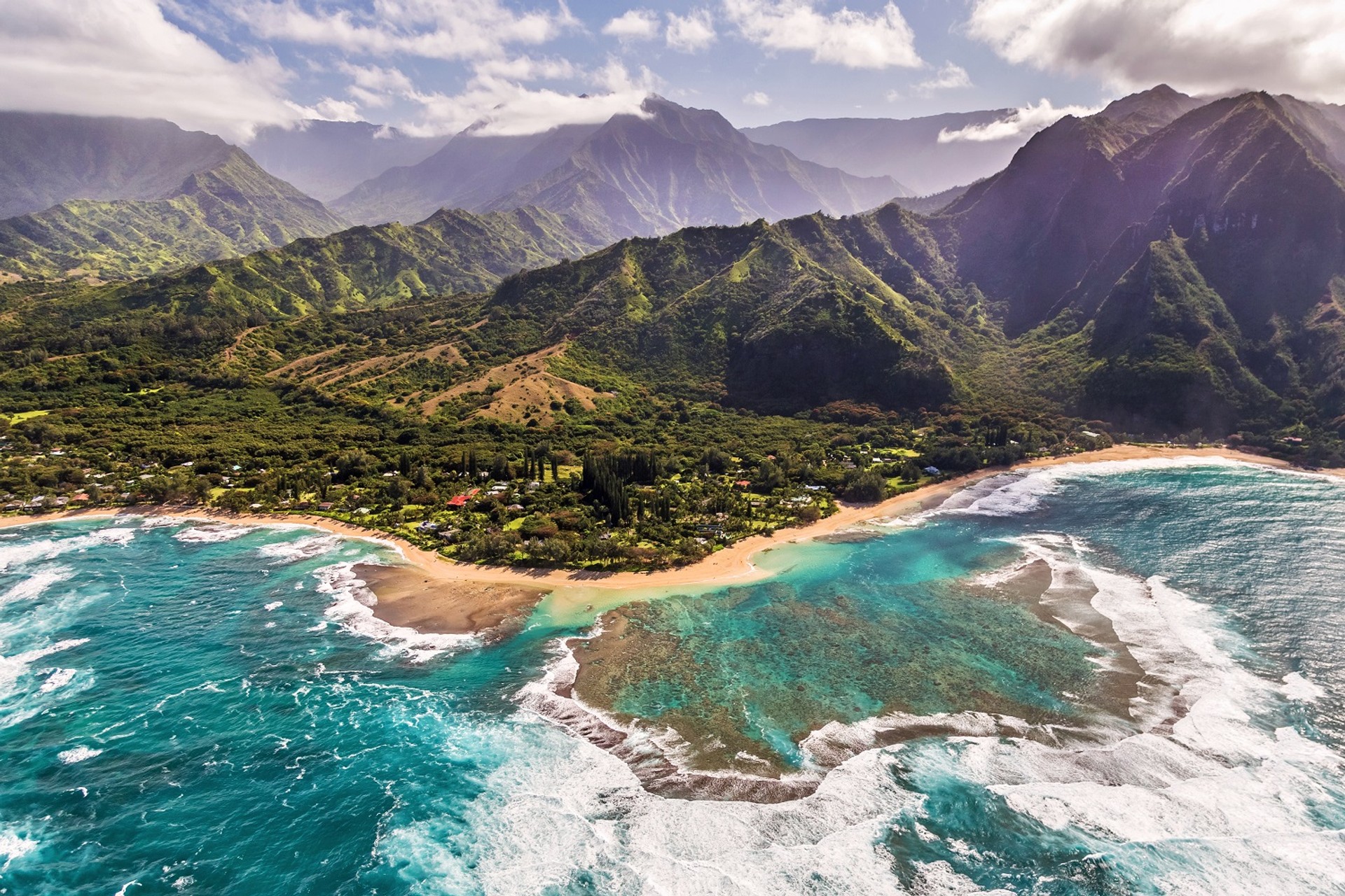 Covered in dramatic, emerald mountains, and lined by 50 miles of white-sand coastline, Kauai is also aptly called 'Garden Island'. Miles of beach lined by turquoise sea water and mountains in the background.