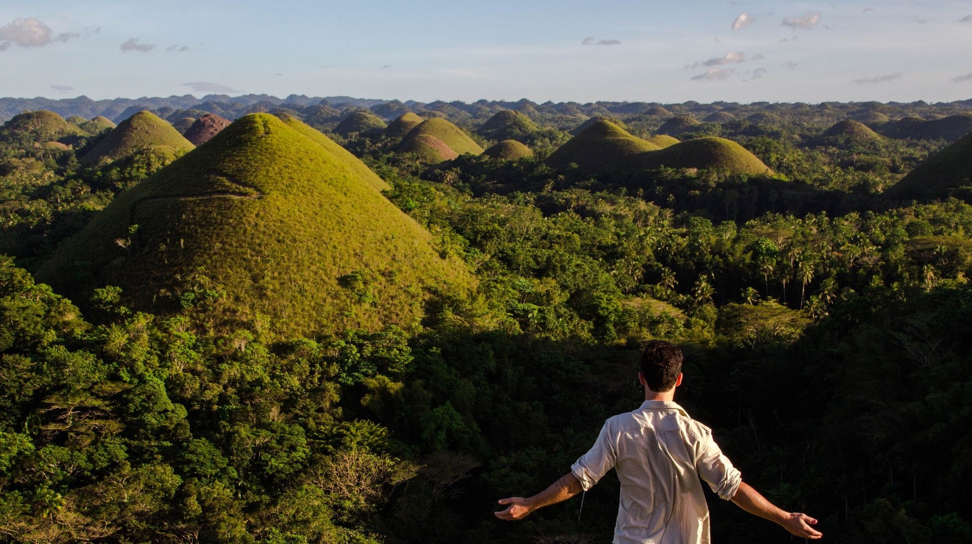 Visit the Chocolate Hills and marvel at this unique geological marvel, where perfectly shaped chocolate-colored hills during your 2 weeks in the Philippines. A man with open arms admiring the beauty of the Chocolate Hills during his 2 weeks in the Philippines.