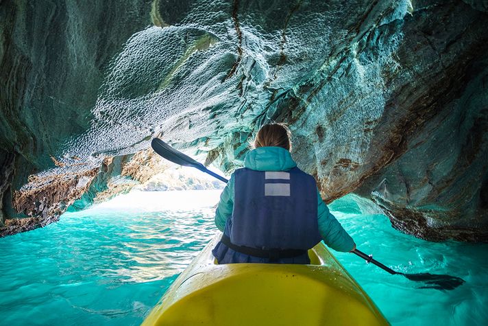 A women kayaks through a cave on turquoise waters