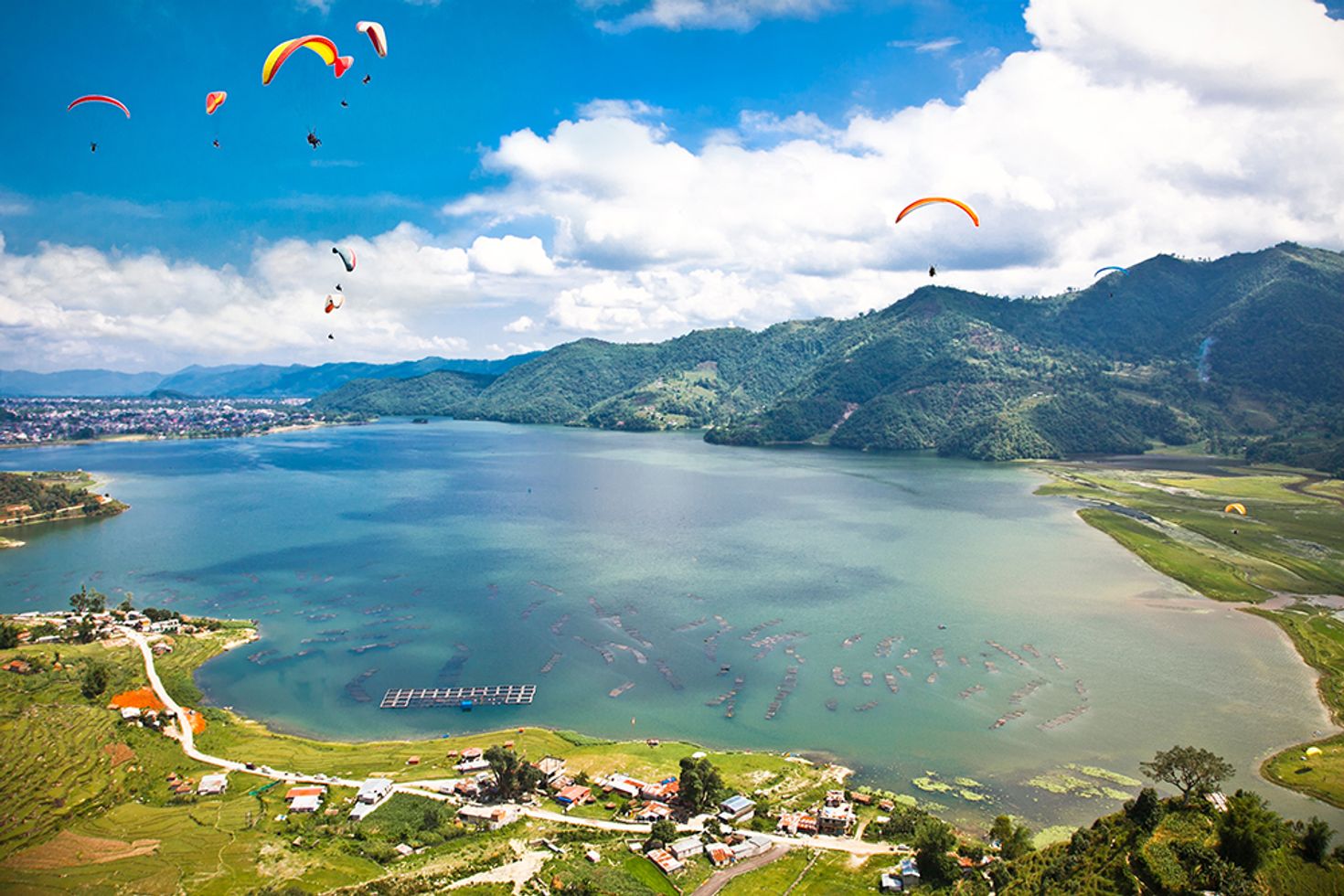 paragliders in the air with a turquoise lake below in Pokhara