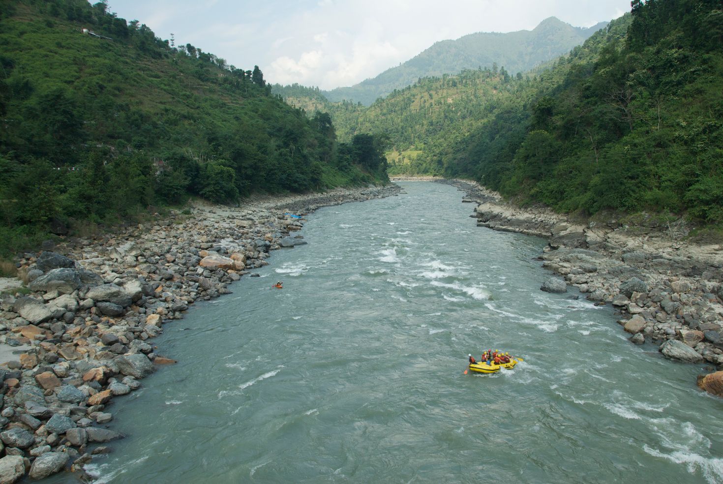 A roaring river runs in between two hills, with a raft afloat in Pokhara