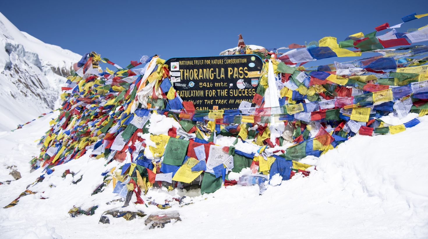 See Thorong La Pass with Buddhist flags while trekking in Nepal.