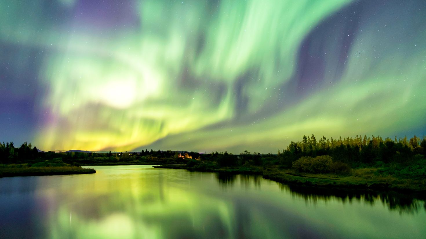 Green and yellow lights in the sky reflecting on the river below