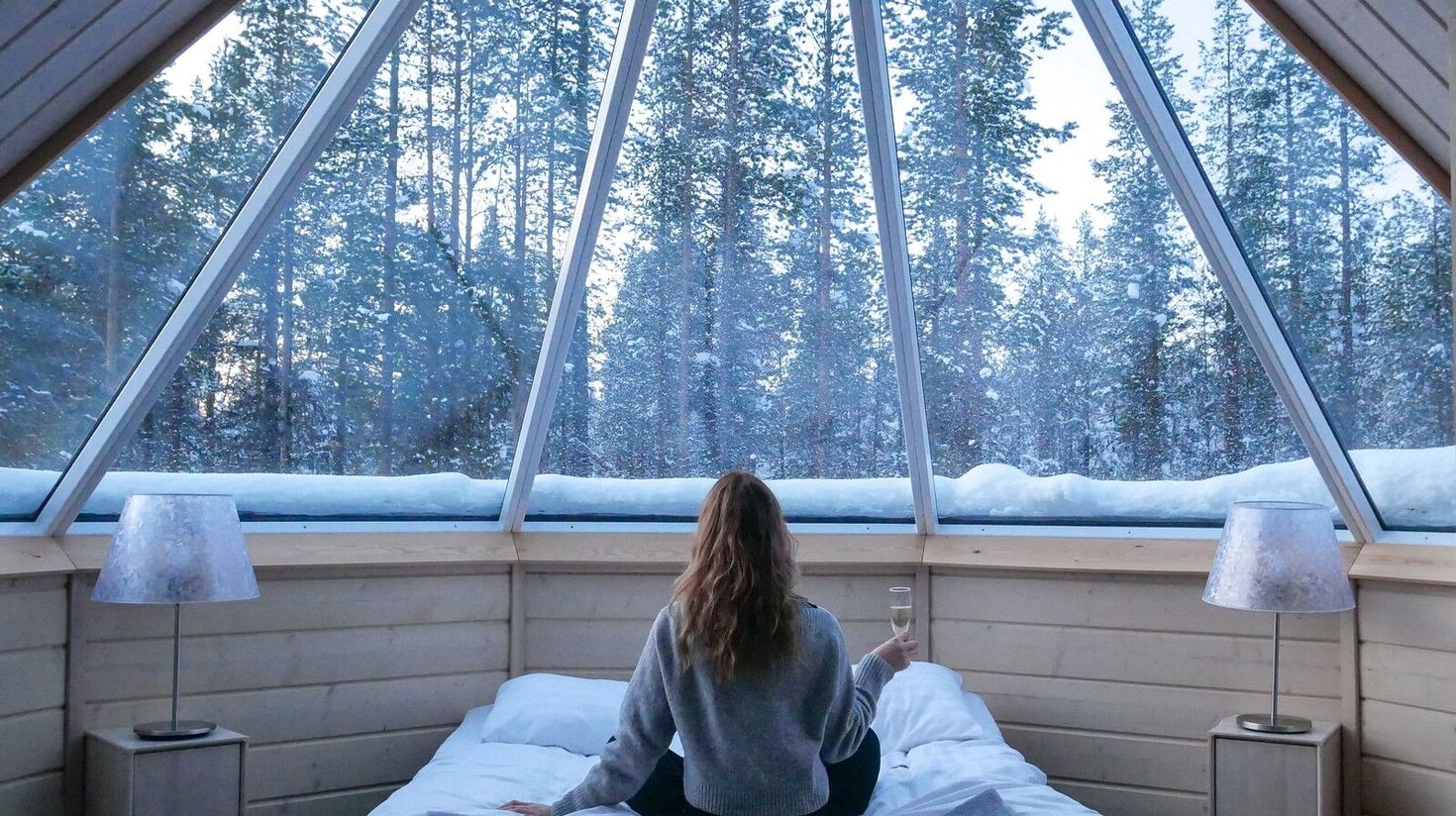 A girl viewing the forest from her hotel room's slanted glass ceilings